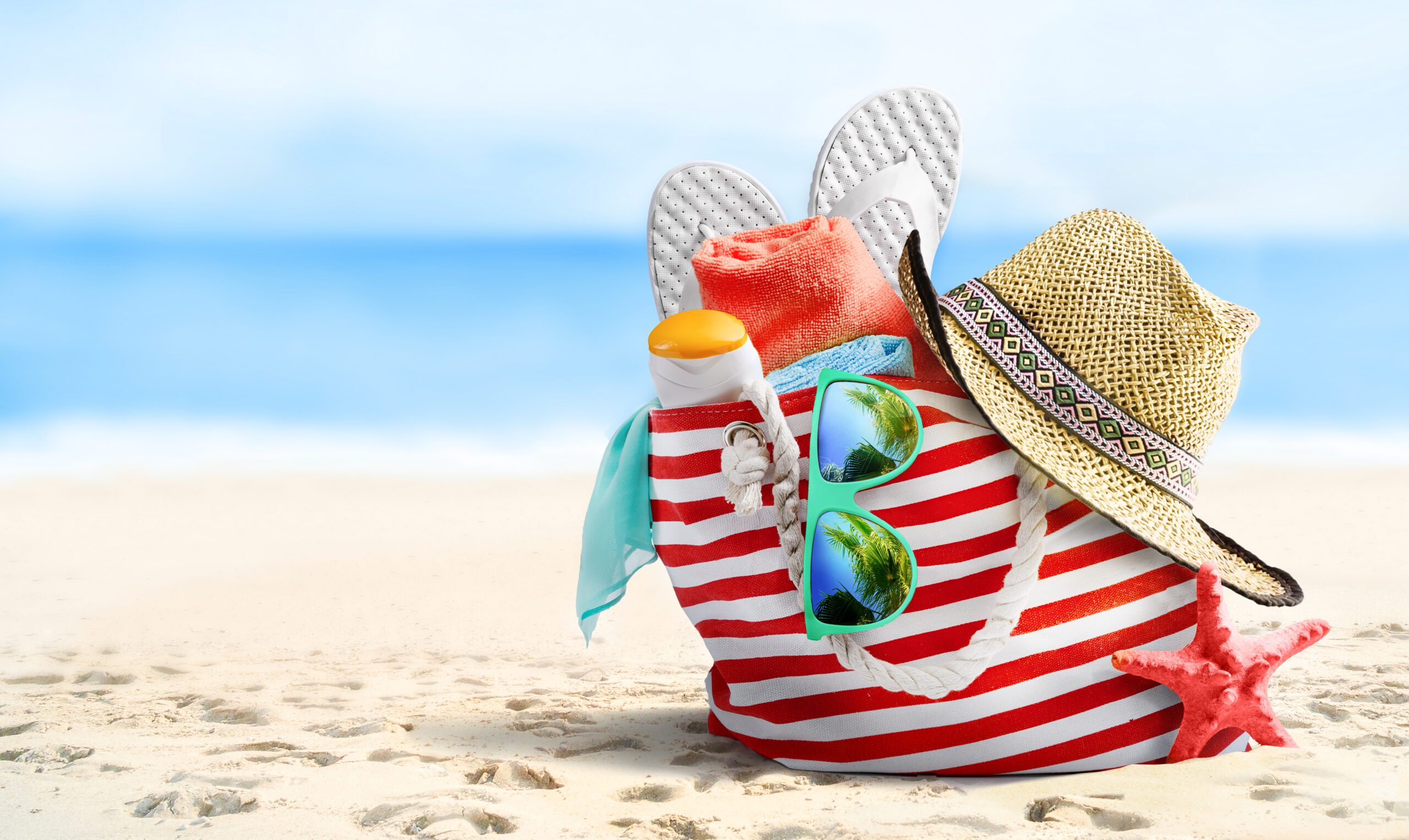 Prelaw summer Summer vacations concept background. Beach bag, straw hat, flip flops, sunglasses and starfish on sandy beach and azure sea on background.